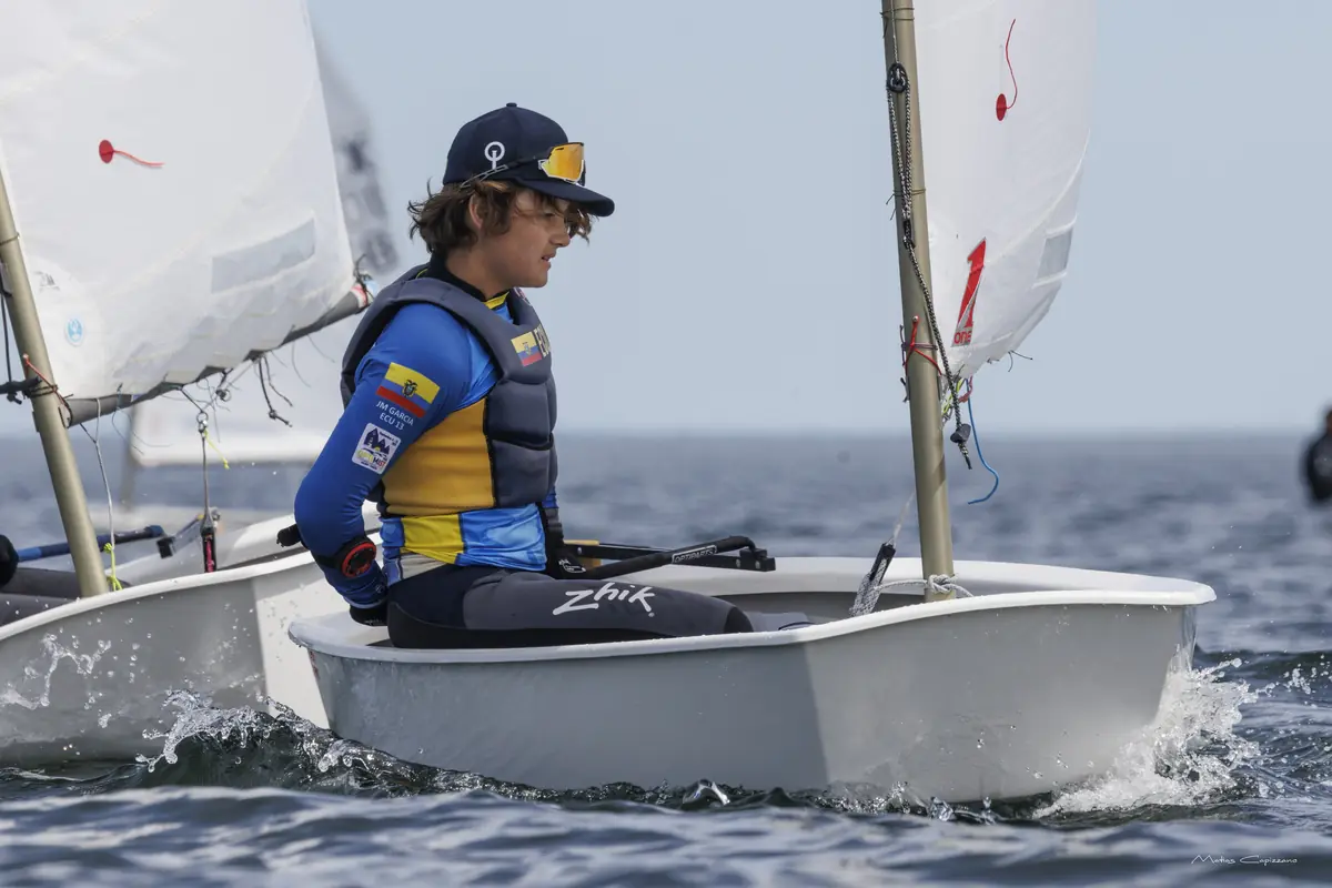 Navegante del equipo ecuatoriano, con la bandera de Ecuador en la manga, avanza en su Optimist levantando espuma.