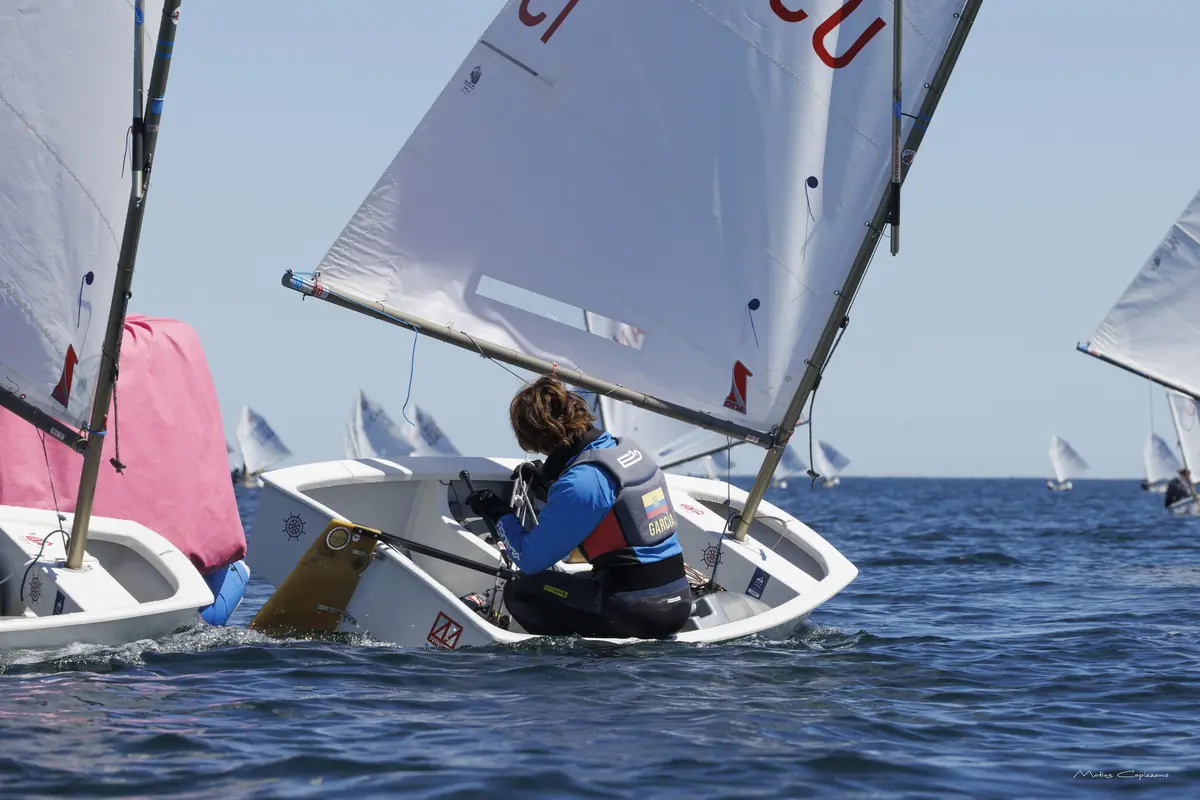 Optimist con vela de Ecuador navegando con la flota internacional al fondo.